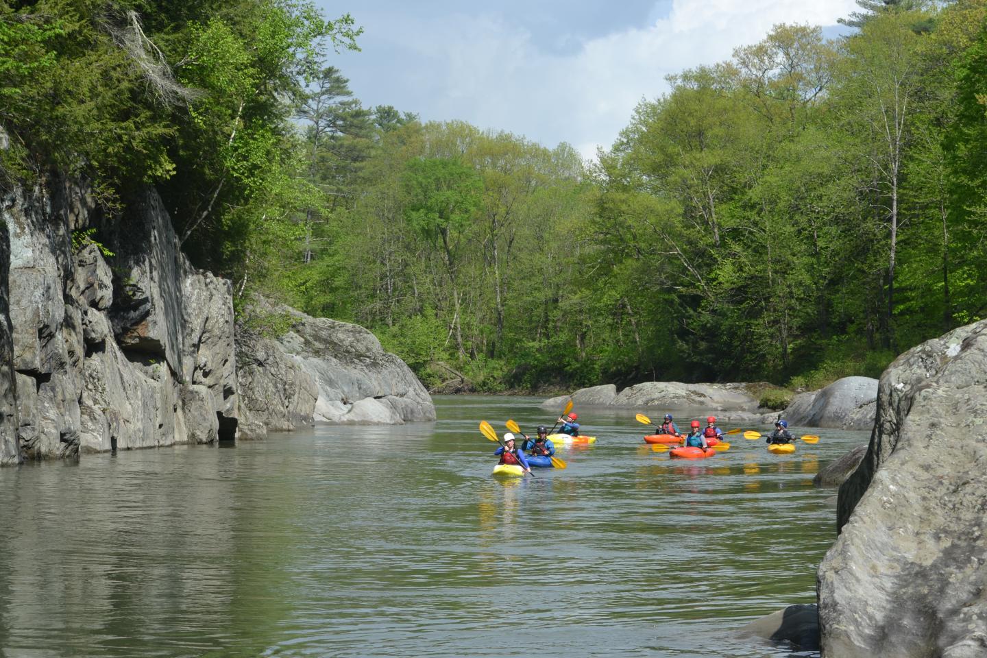 Kayakers paddle down a serene river surrounded by lush greenery and rocks.