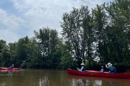 Red canoes on a calm river, surrounded by trees under a cloudy sky.