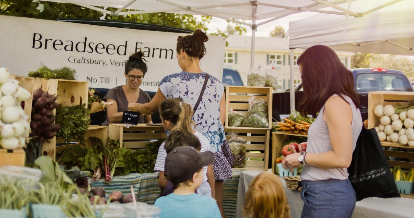 Farmers' market stand with people buying fresh produce.