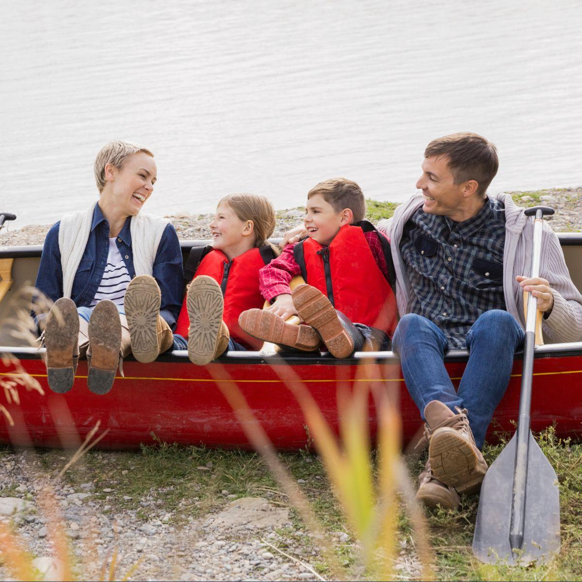 Family sitting in a red canoe, smiling by the water.
