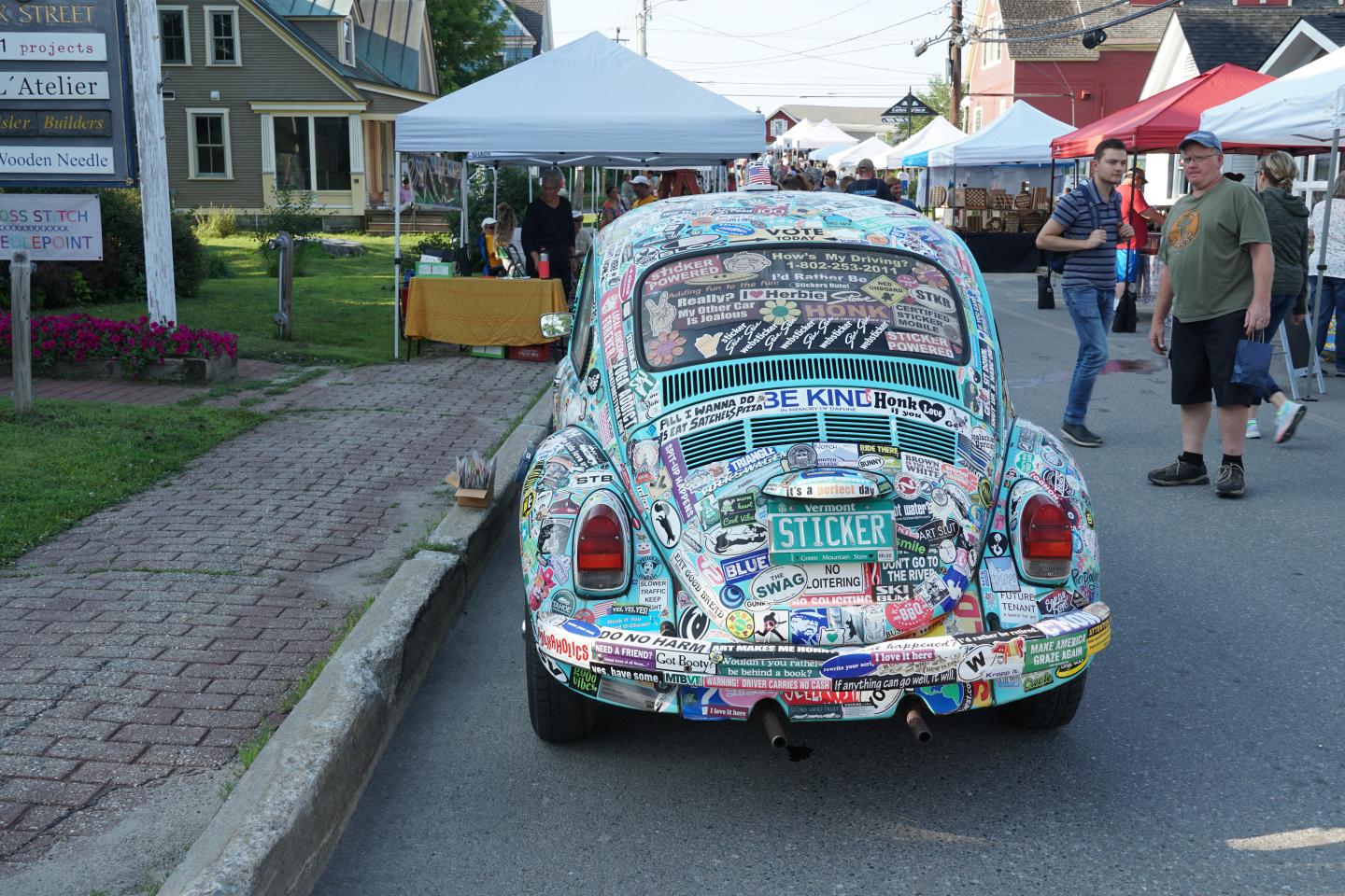 Vintage VW Beetle covered in colorful stickers at a street market.