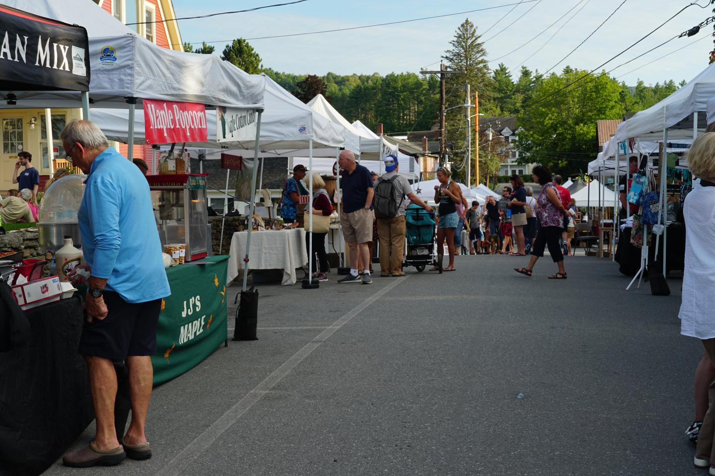 Crowded outdoor market with vendor tents and people browsing.