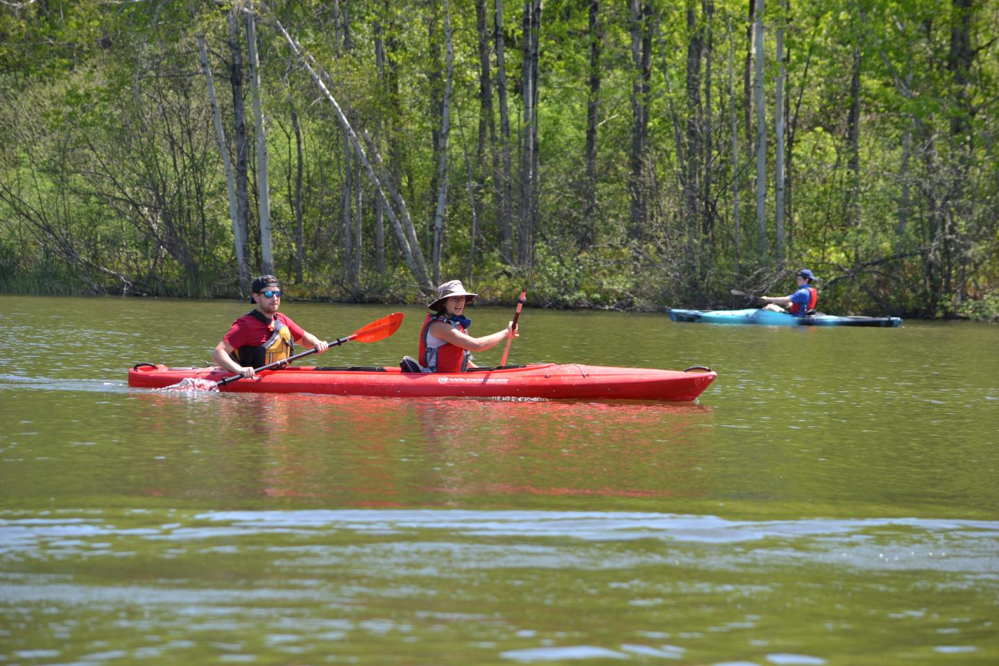 Two people kayaking on a calm lake surrounded by trees.