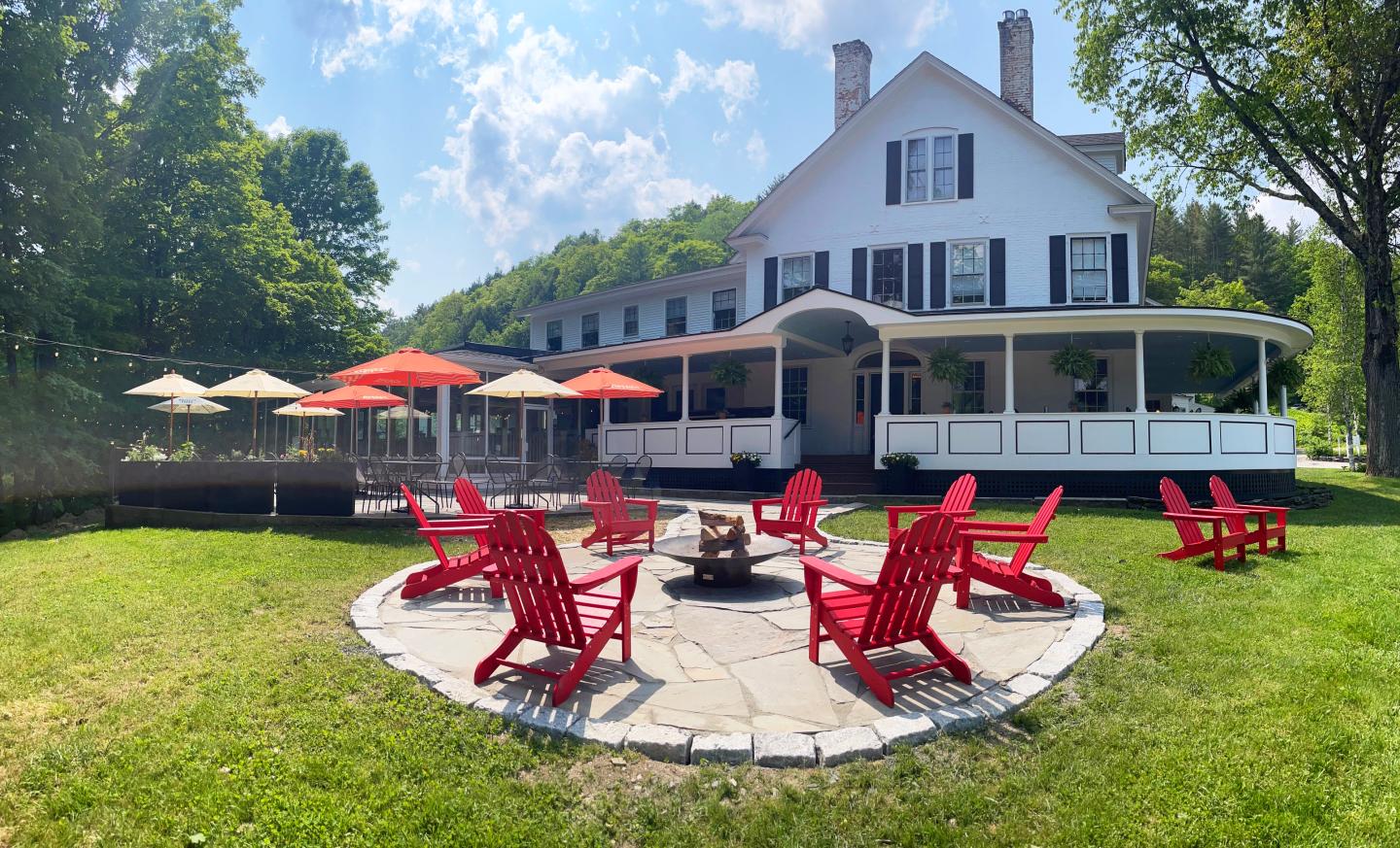 Large white house with red chairs and umbrellas on a sunny day.