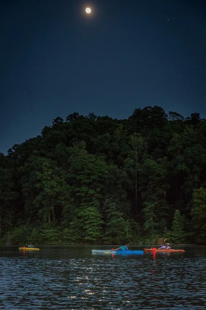 Kayakers on lake at night under moonlit sky.