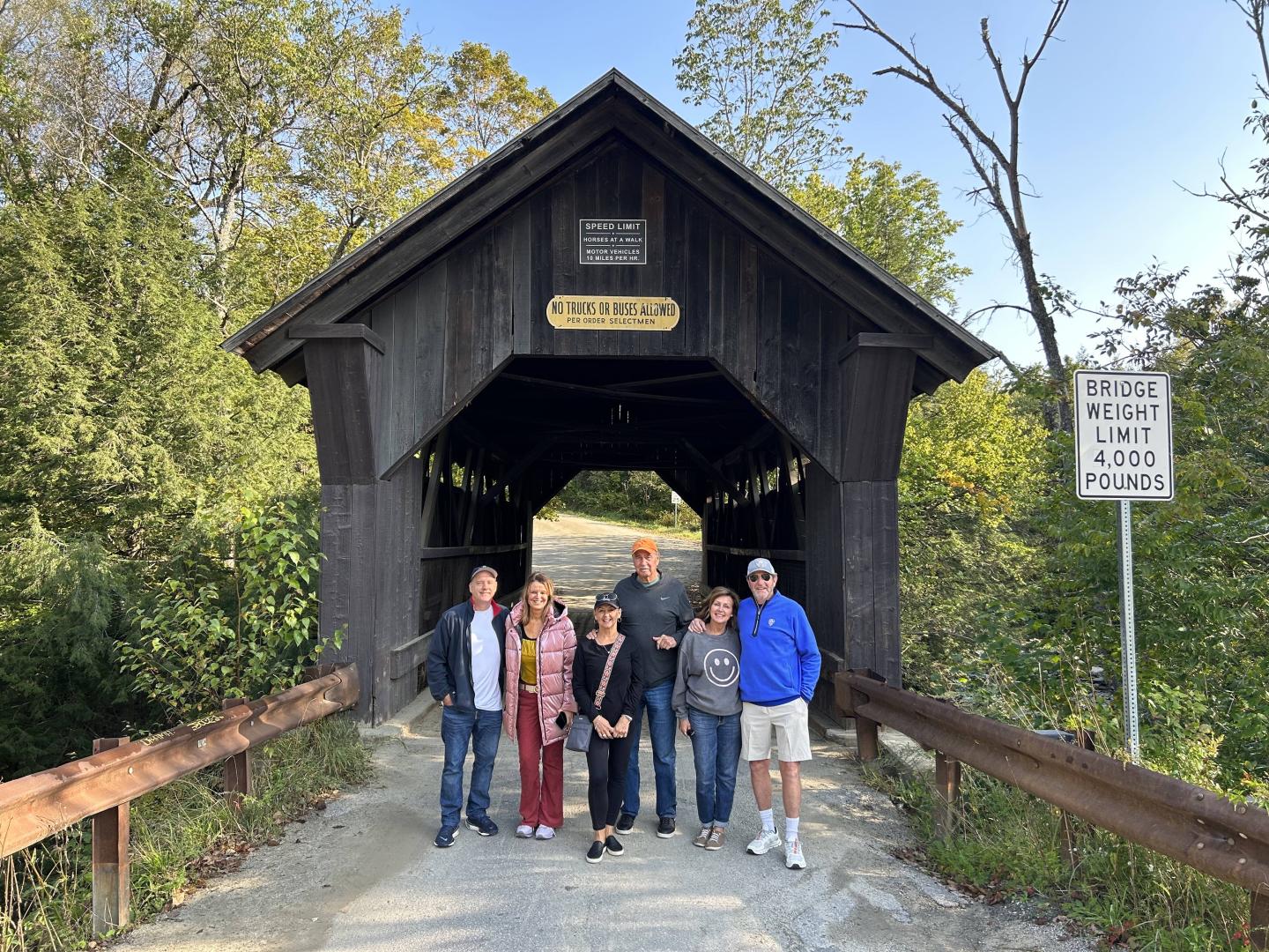 Group of people standing in front of a wooden covered bridge.