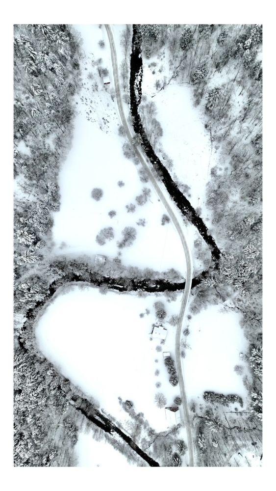 Snow-covered landscape with winding road through trees.