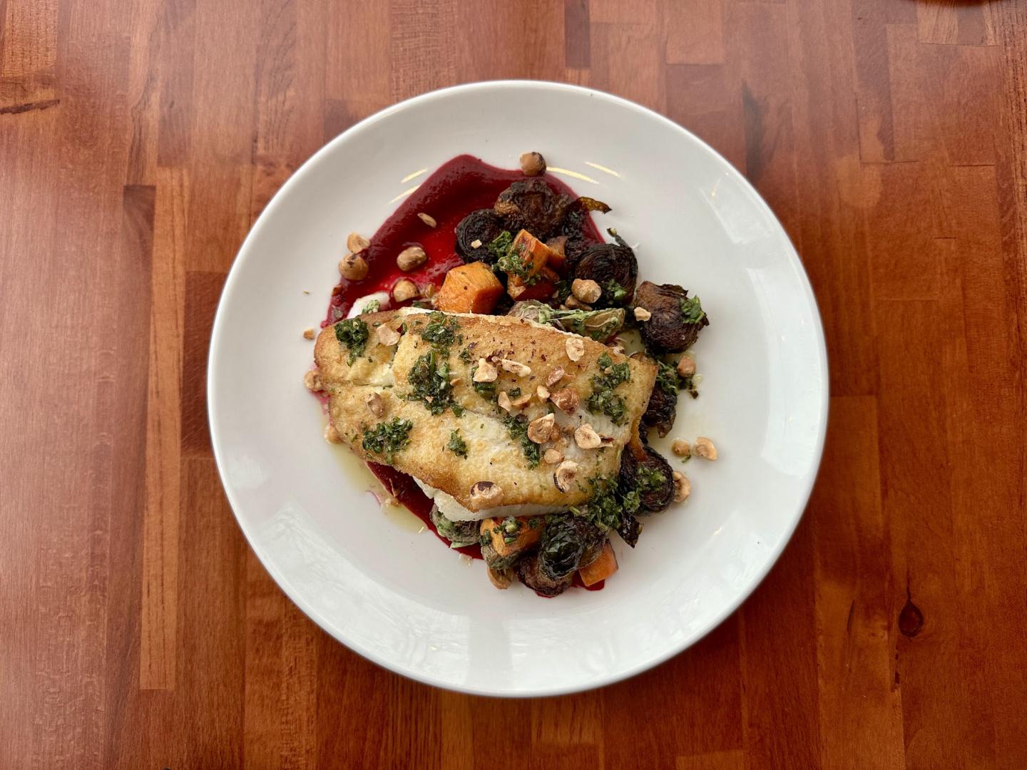 Grilled fish with vegetables and sauce on a white plate.
