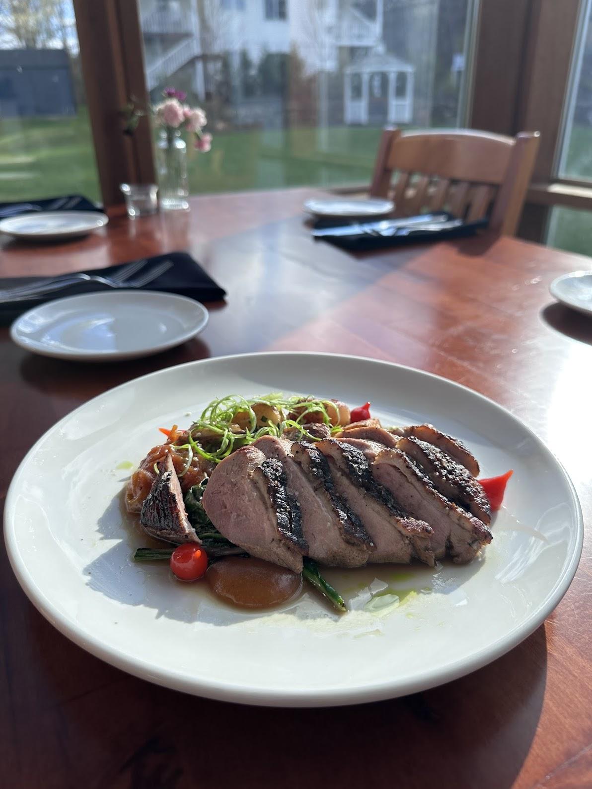 Sliced duck on a plate with vegetables in a sunlit dining room.