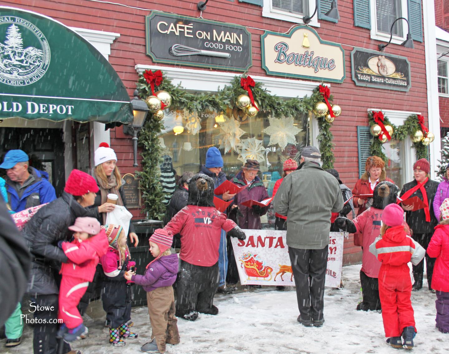 Crowd in winter clothing gathered outside decorated shops in snowy street.
