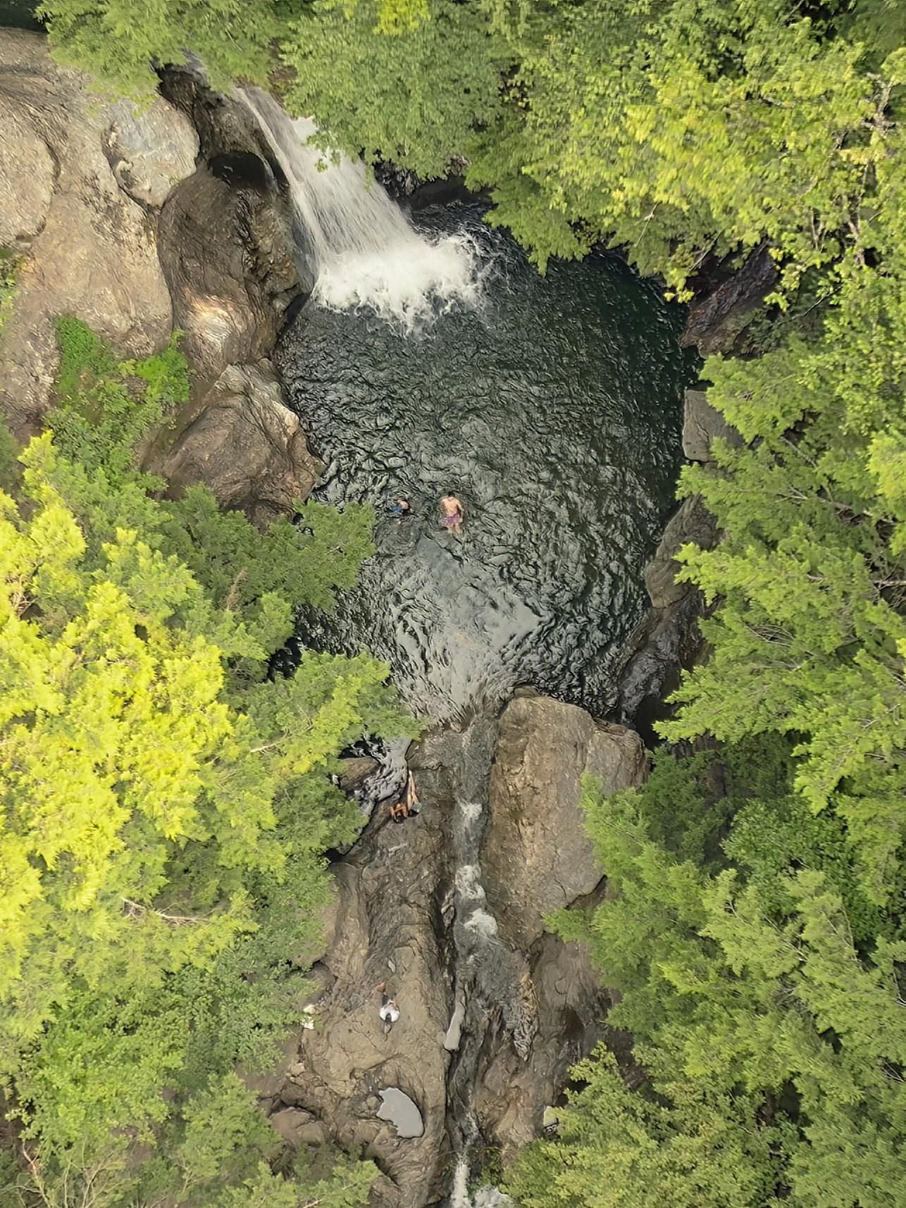 Waterfall pool surrounded by green trees, seen from above.
