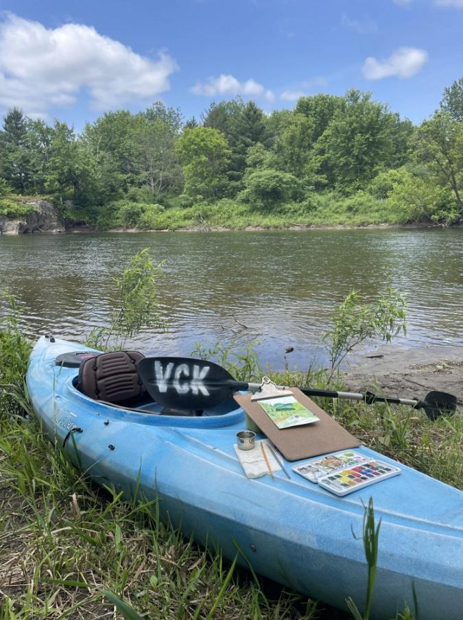 Blue kayak on grassy riverbank with trees in the background.