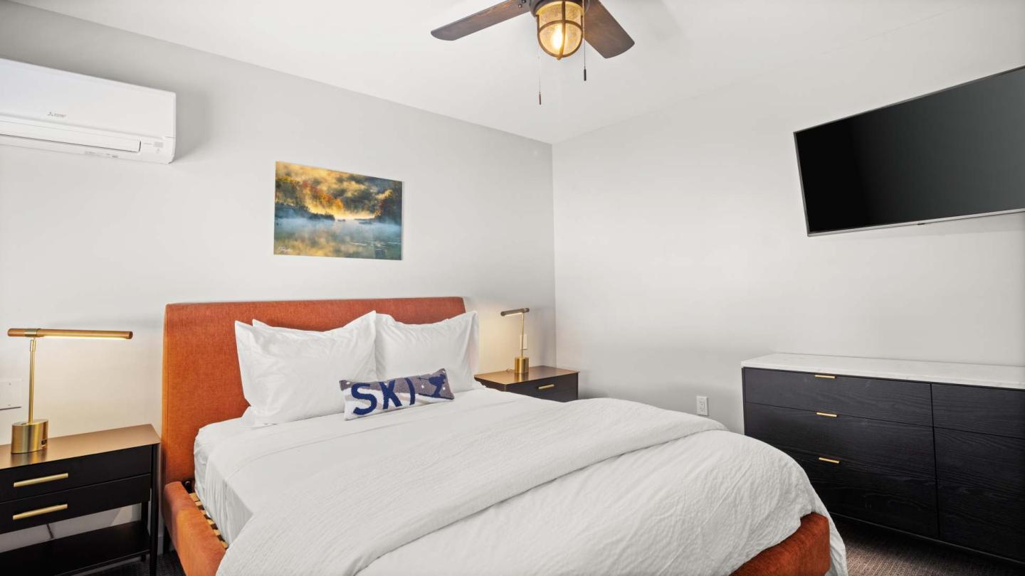Cozy bedroom with white bedding, painting, and wall-mounted TV.