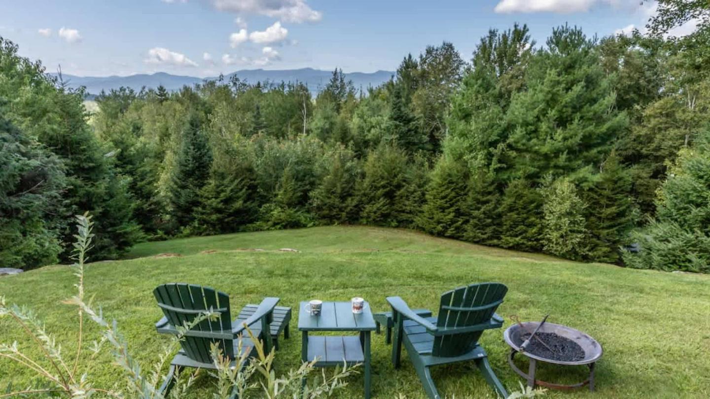 Four green chairs and a table overlooking lush trees and distant mountains.