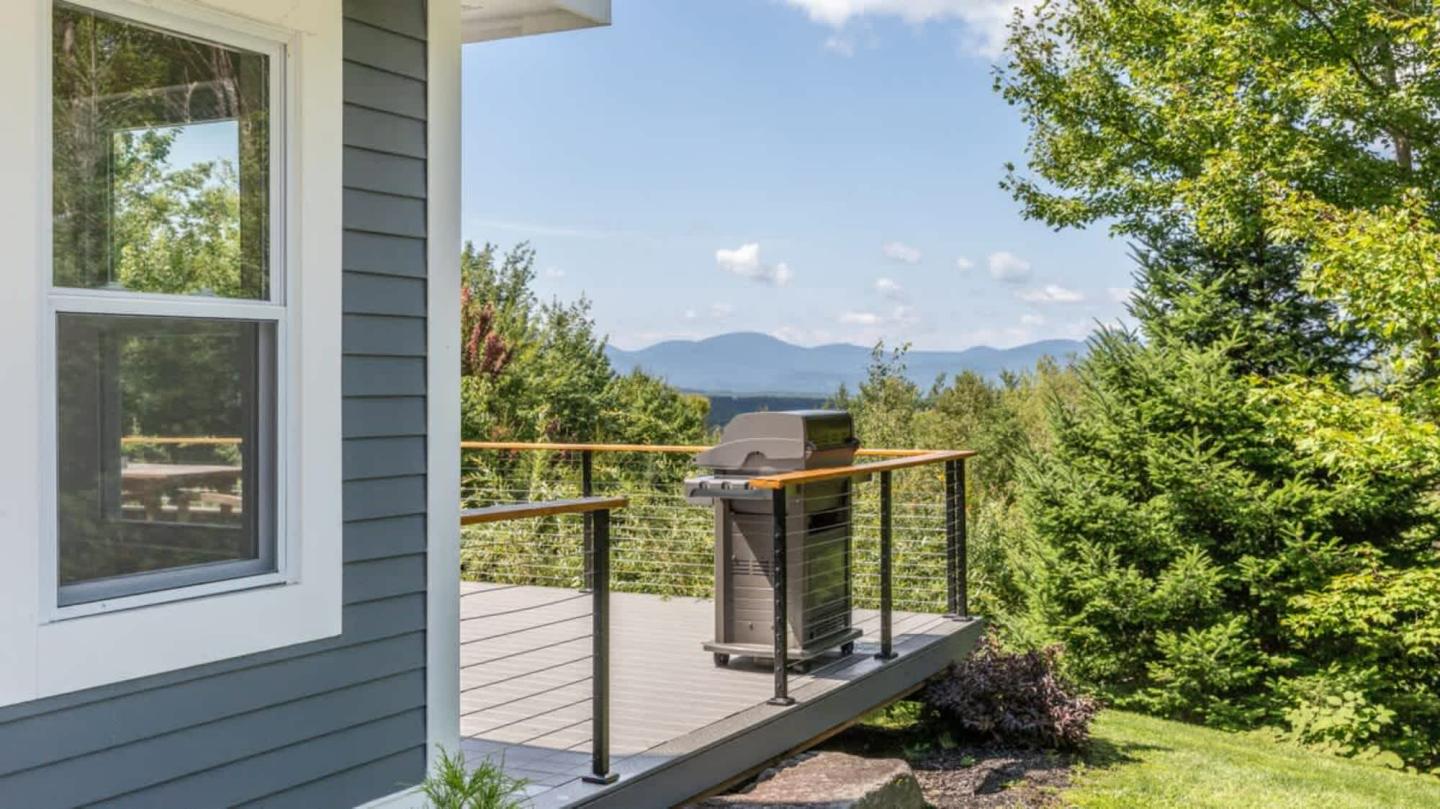 House deck with a grill, overlooking trees and distant mountains.