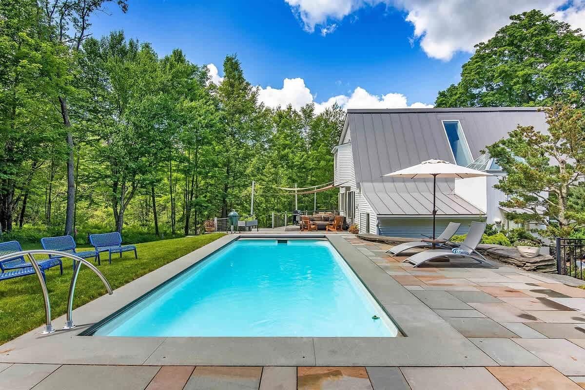 Modern house with a pool, lawn chairs, and umbrella on a sunny day.
