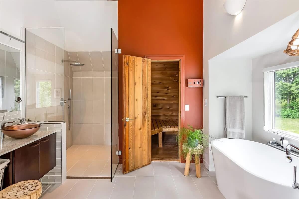 Modern bathroom with a glass shower, wooden sauna door, and freestanding tub.