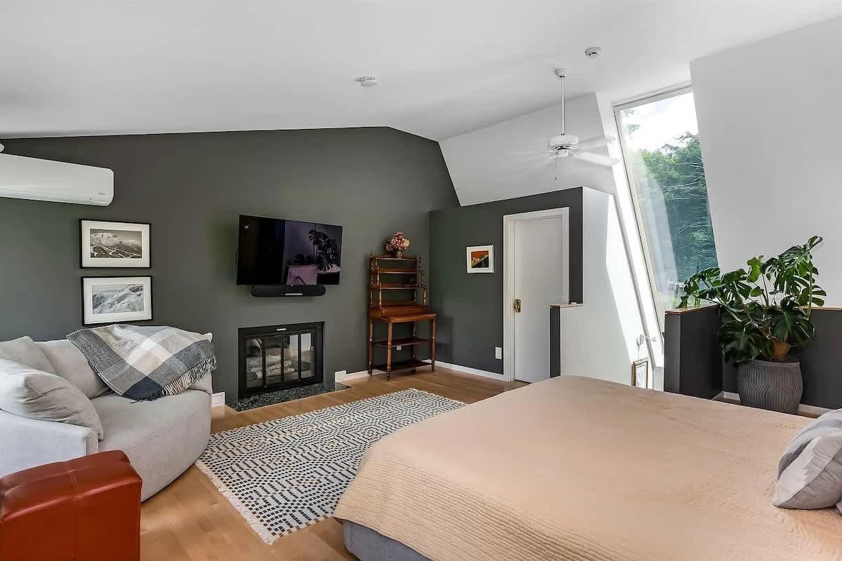 Spacious bedroom with gray accent wall, bed, sofa, rug, and large window.