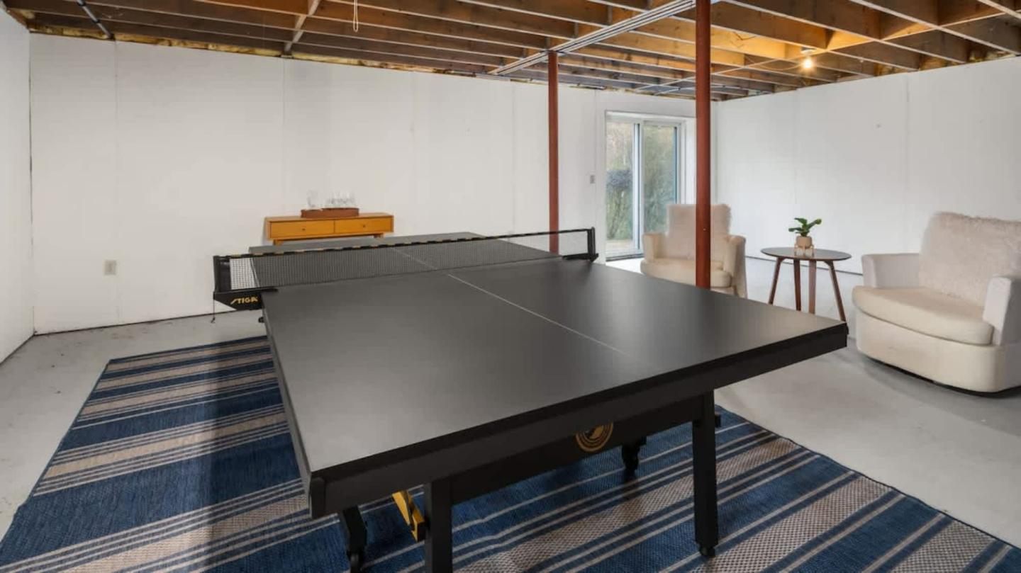 Table tennis setup in a basement with chairs and a small table.