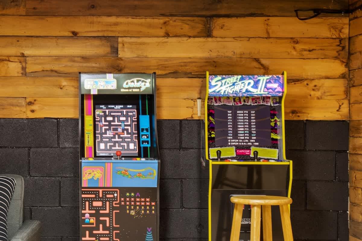 Vintage arcade games in a wooden and brick interior, one with a stool.