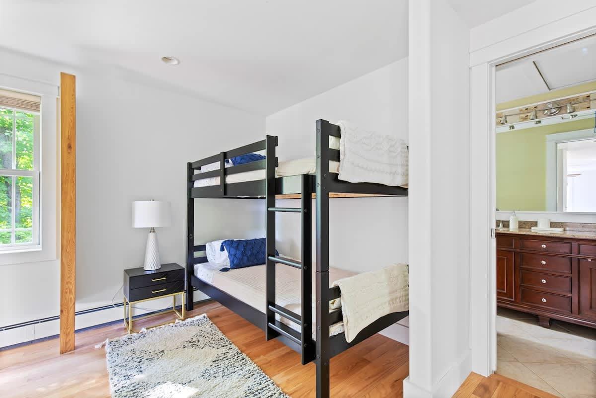 Bunk beds in a bright room, next to window, lamp on bedside table.
