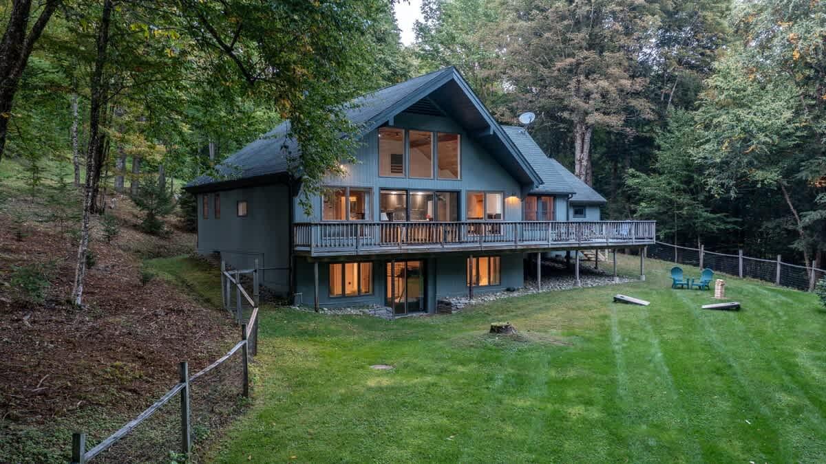 Wooden house with large windows in a forest clearing.