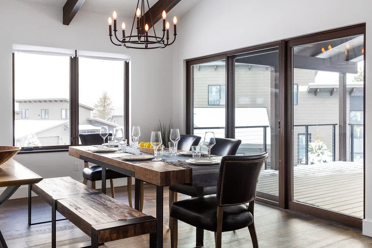 Rustic dining room with wooden table, black chairs, and chandelier, near large windows.