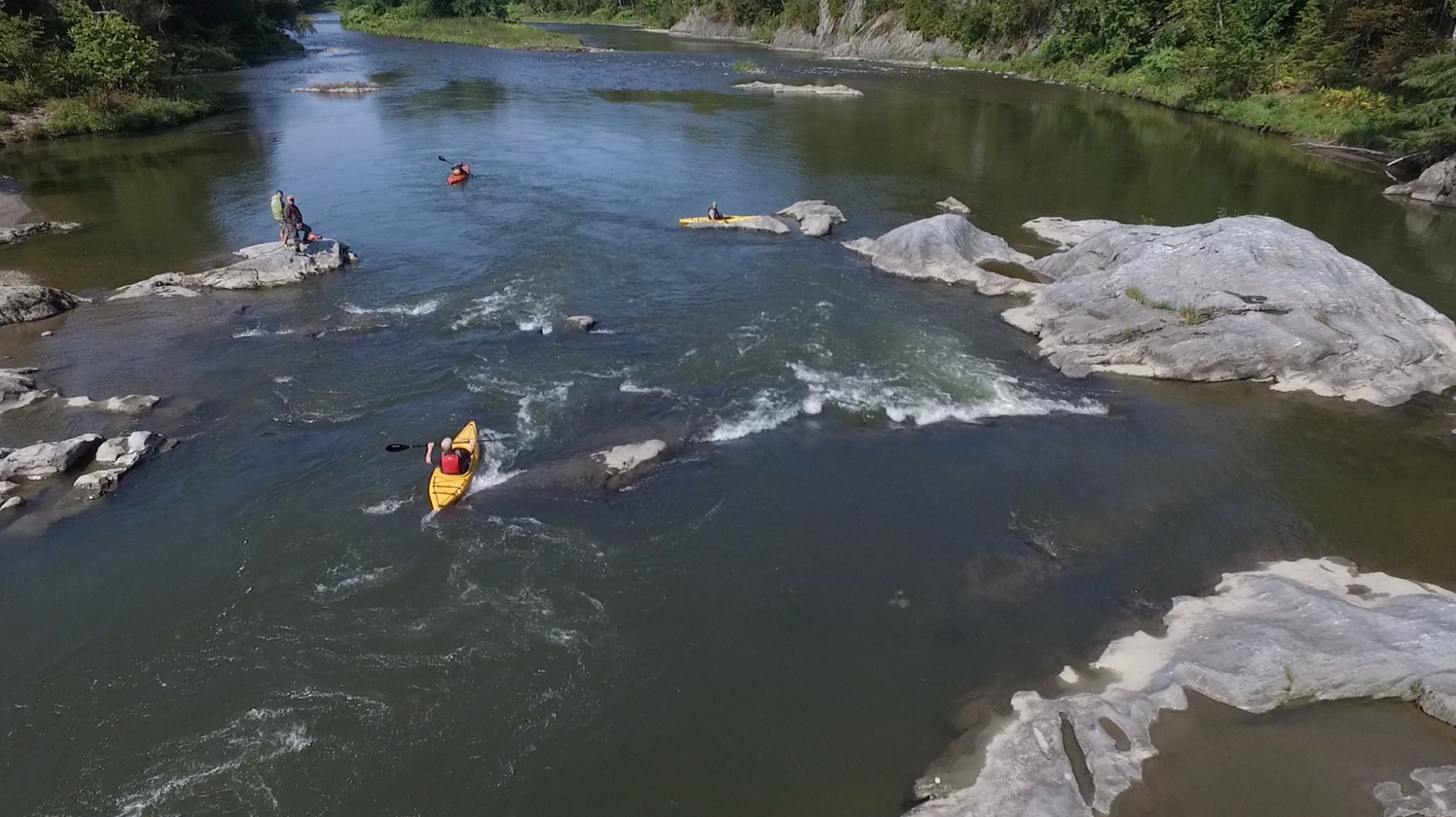 Kayakers navigate a rapids under a clear blue sky.