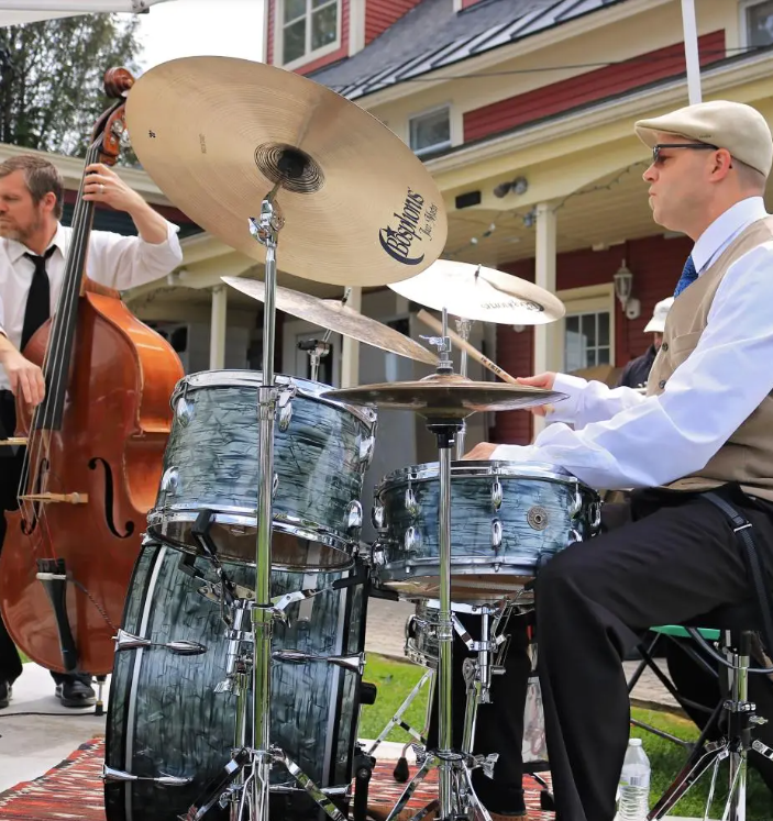 Musicians playing drums and double bass outdoors, wearing formal attire.