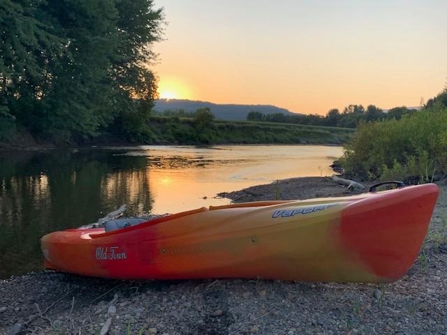Orange kayak on a riverbank at sunset.