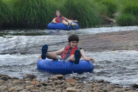 Two people tubing down a river in blue tubes, wearing life jackets.