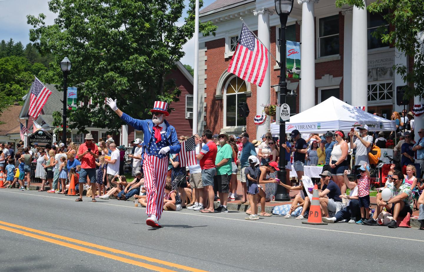 Parade with Uncle Sam performer, crowd, and American flags.