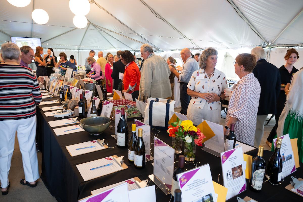 A bustling auction with people mingling under a white tent.