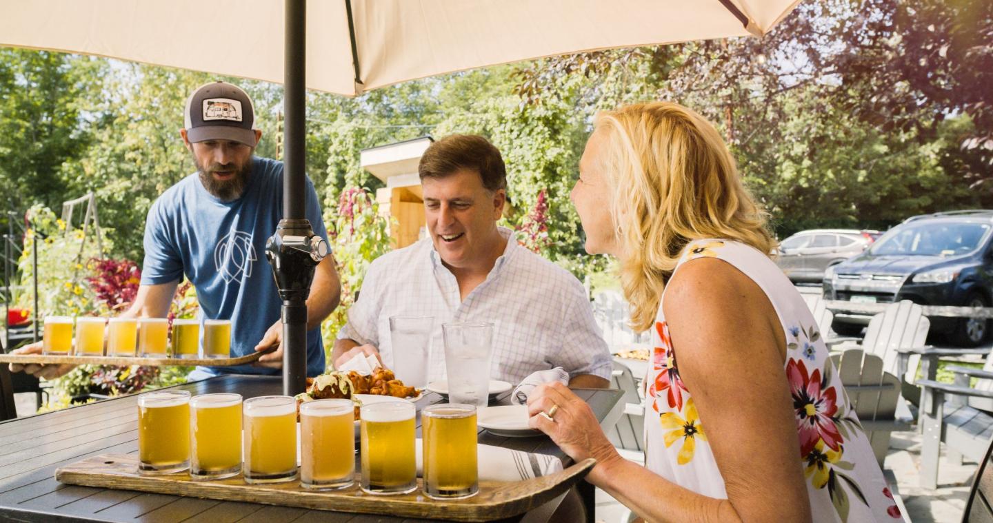 Outdoor dining with friends enjoying drinks under a large umbrella.