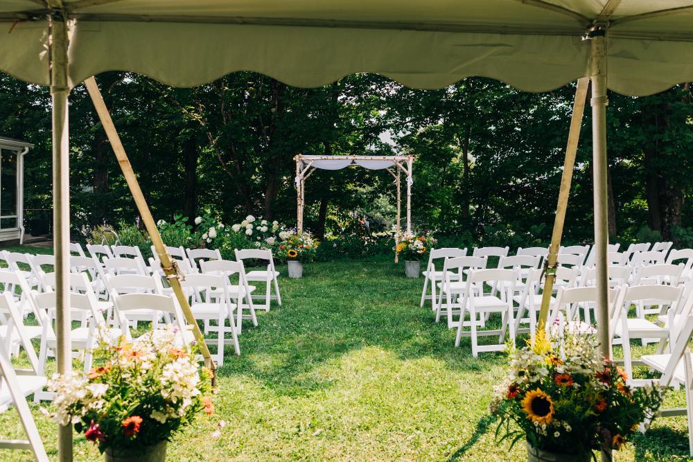 Outdoor wedding setup with white chairs and floral decorations under a canopy.