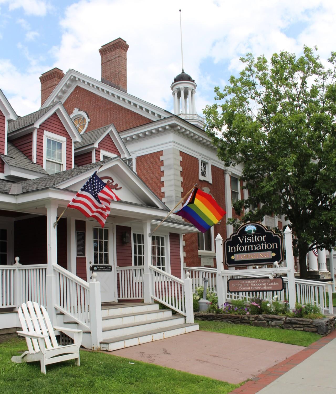 Red brick house with American and rainbow flags, white porch, green lawn.