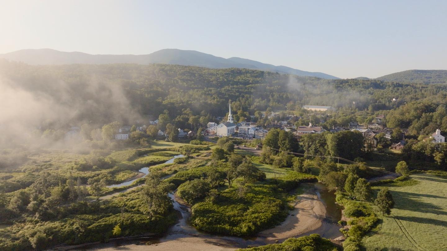 Aerial view of a village surrounded by lush greenery and misty mountains.