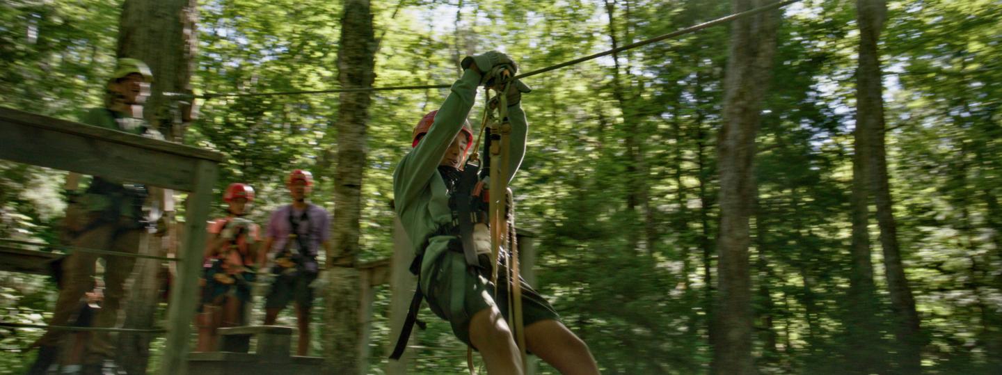 Person zip-lining through lush forest, others watch from platform.