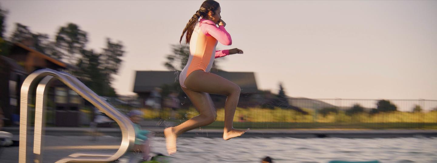 Girl jumping into a lake from a dock, wearing a bright swimsuit.