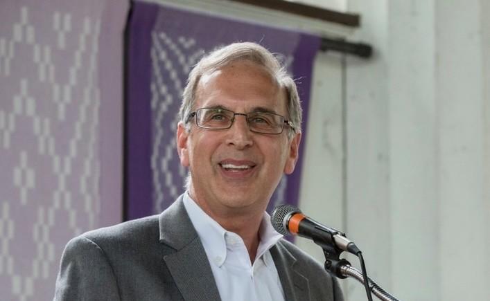 Man in a suit speaking at a microphone, smiling.