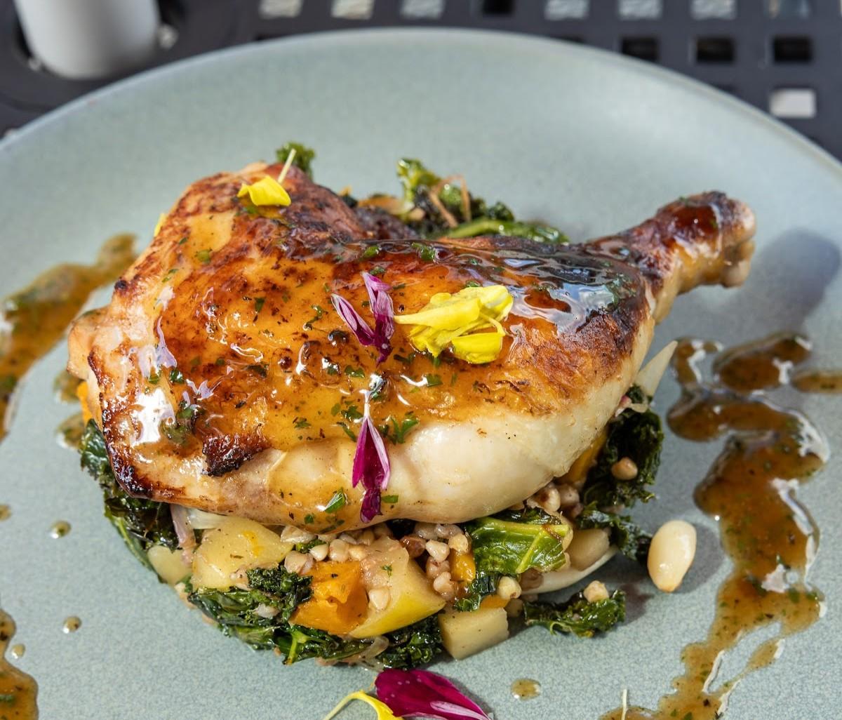 Roasted chicken leg with greens and garnish on a blue plate.