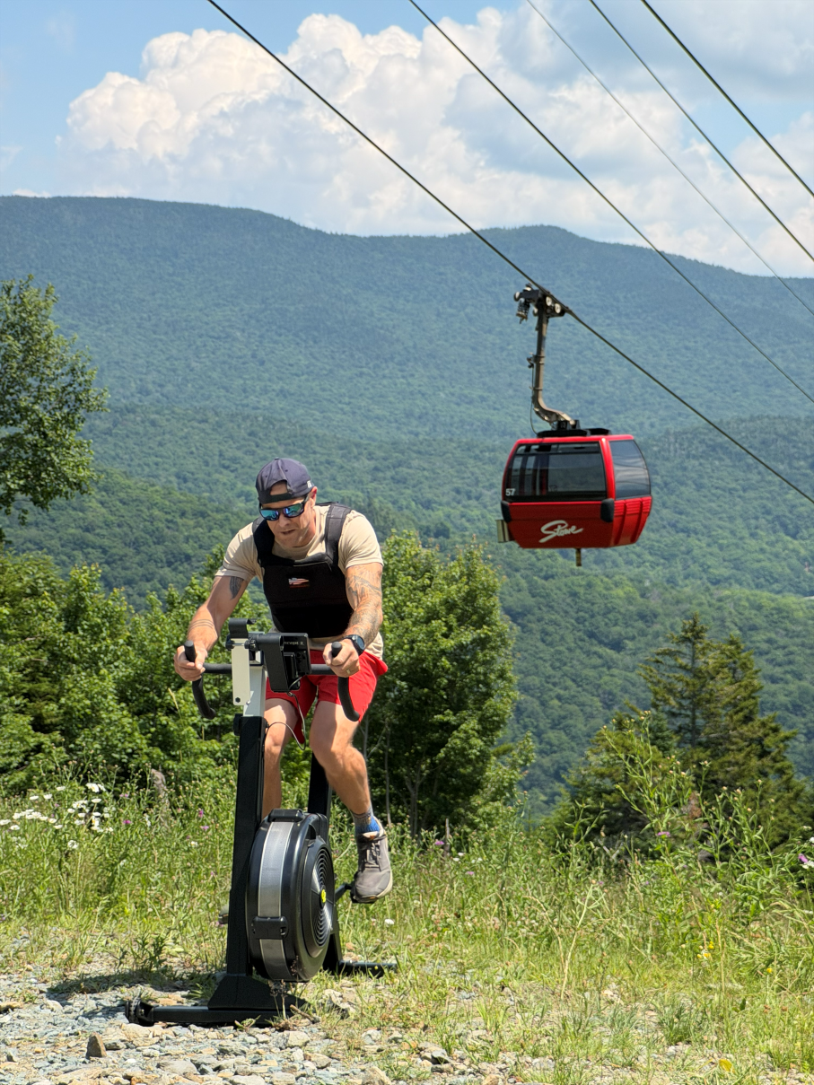 Man cycling outdoors with mountains and a red gondola in the background.