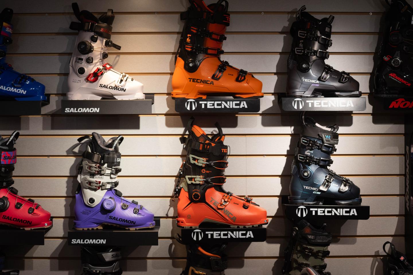 Ski boots displayed on a wall, arranged by color and brand.