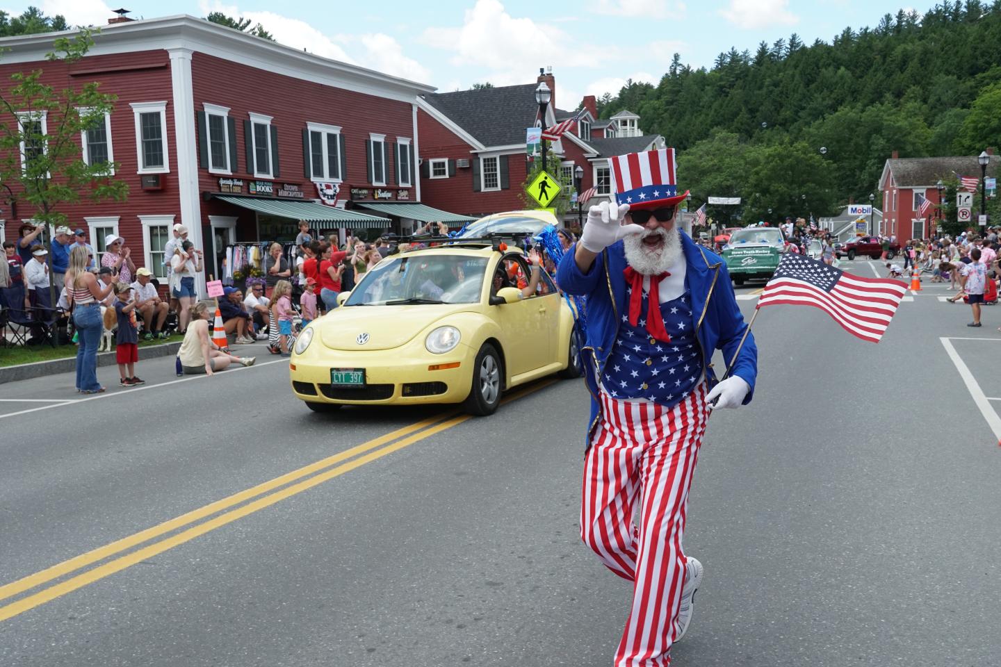 Parade with Uncle Sam costume, waving flag, yellow car behind.