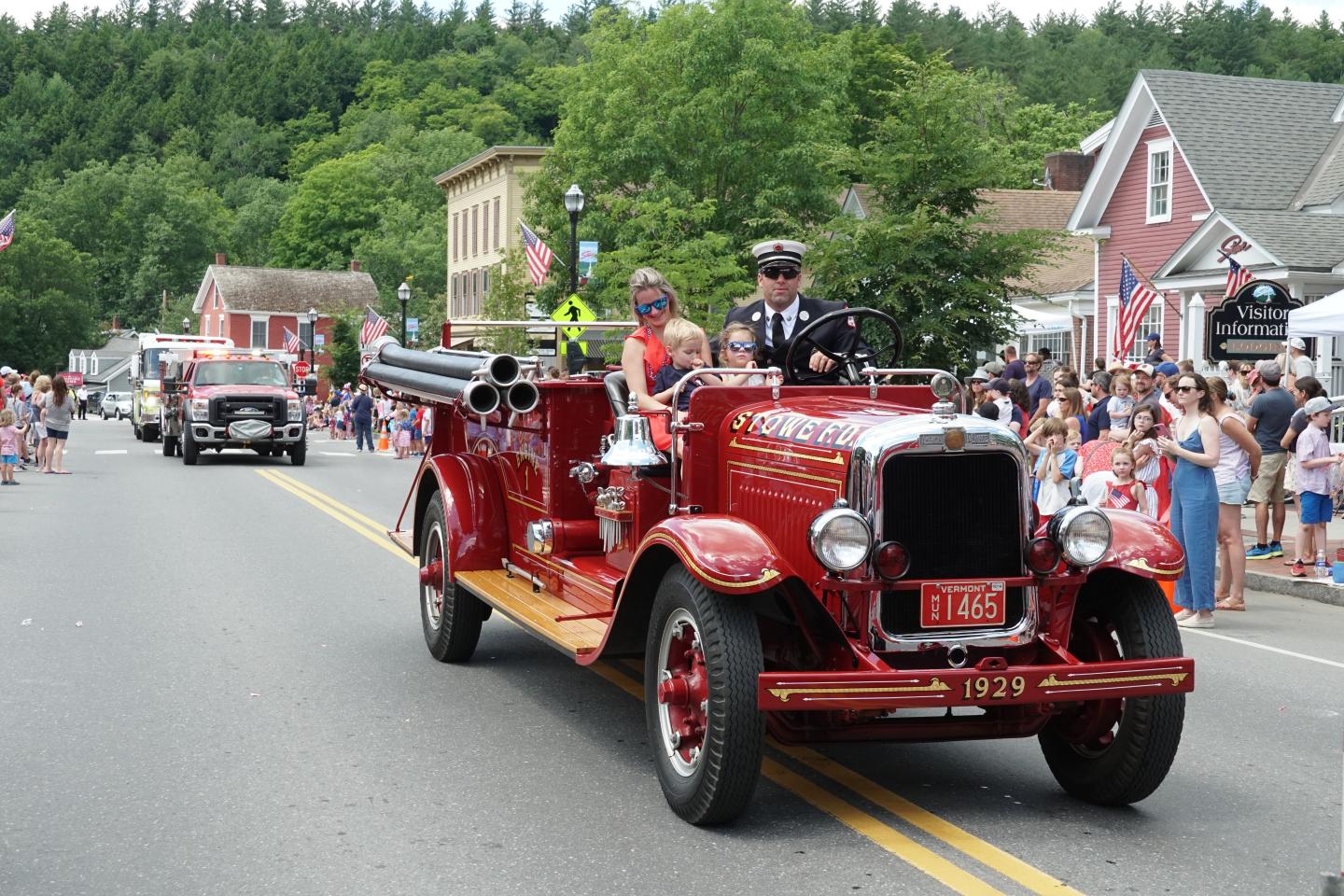 Historic red fire truck in a parade on a tree-lined street.