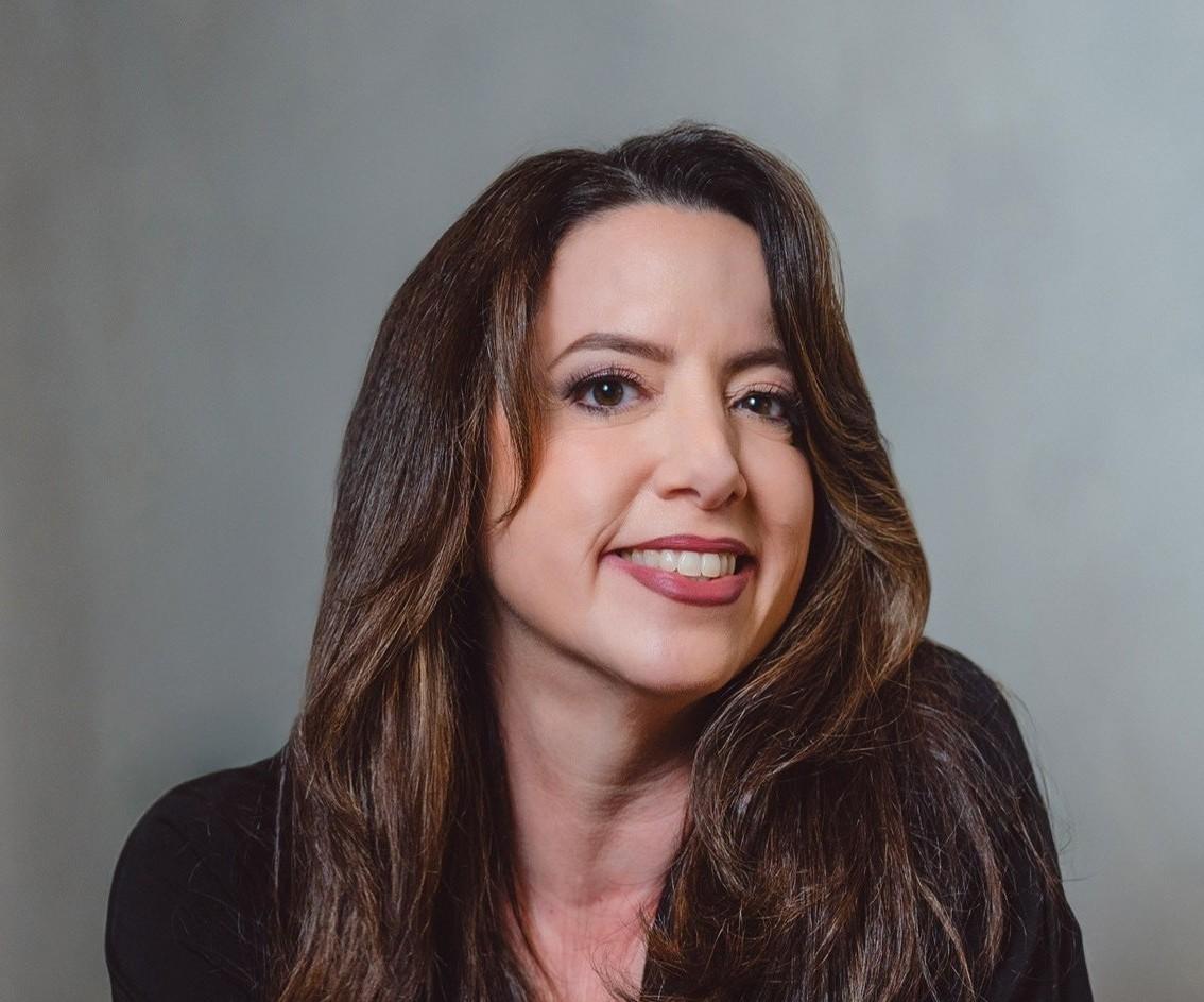 Smiling woman with long brown hair against a gray background.