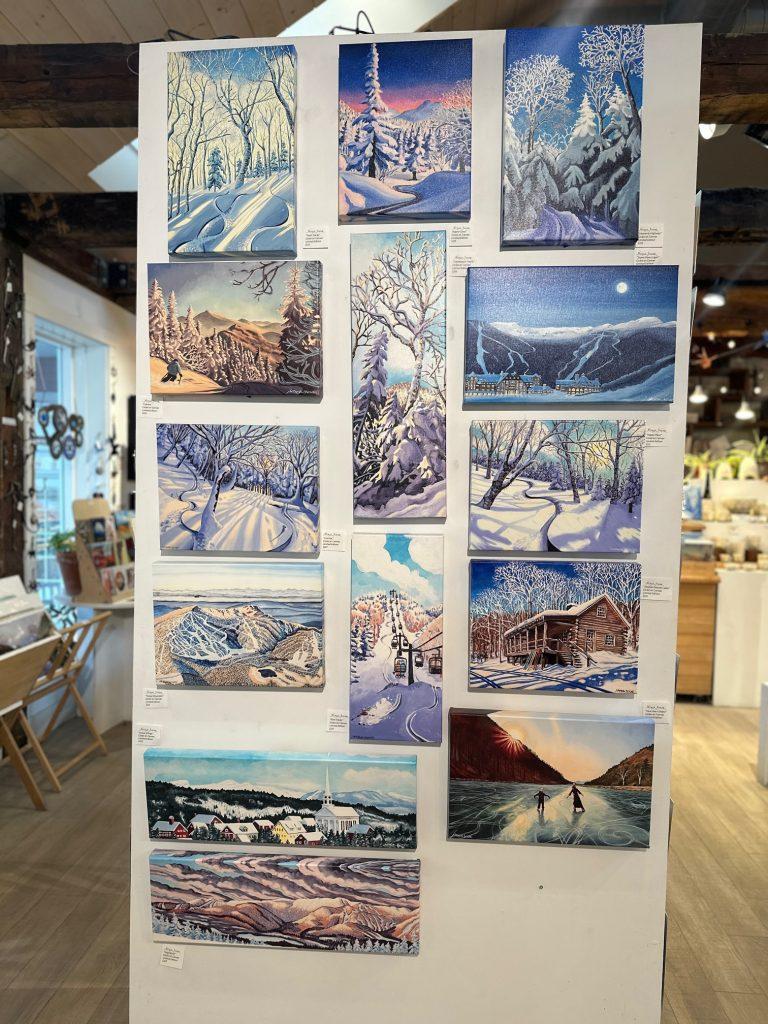 Wall display of winter landscape paintings in a cozy gallery space.