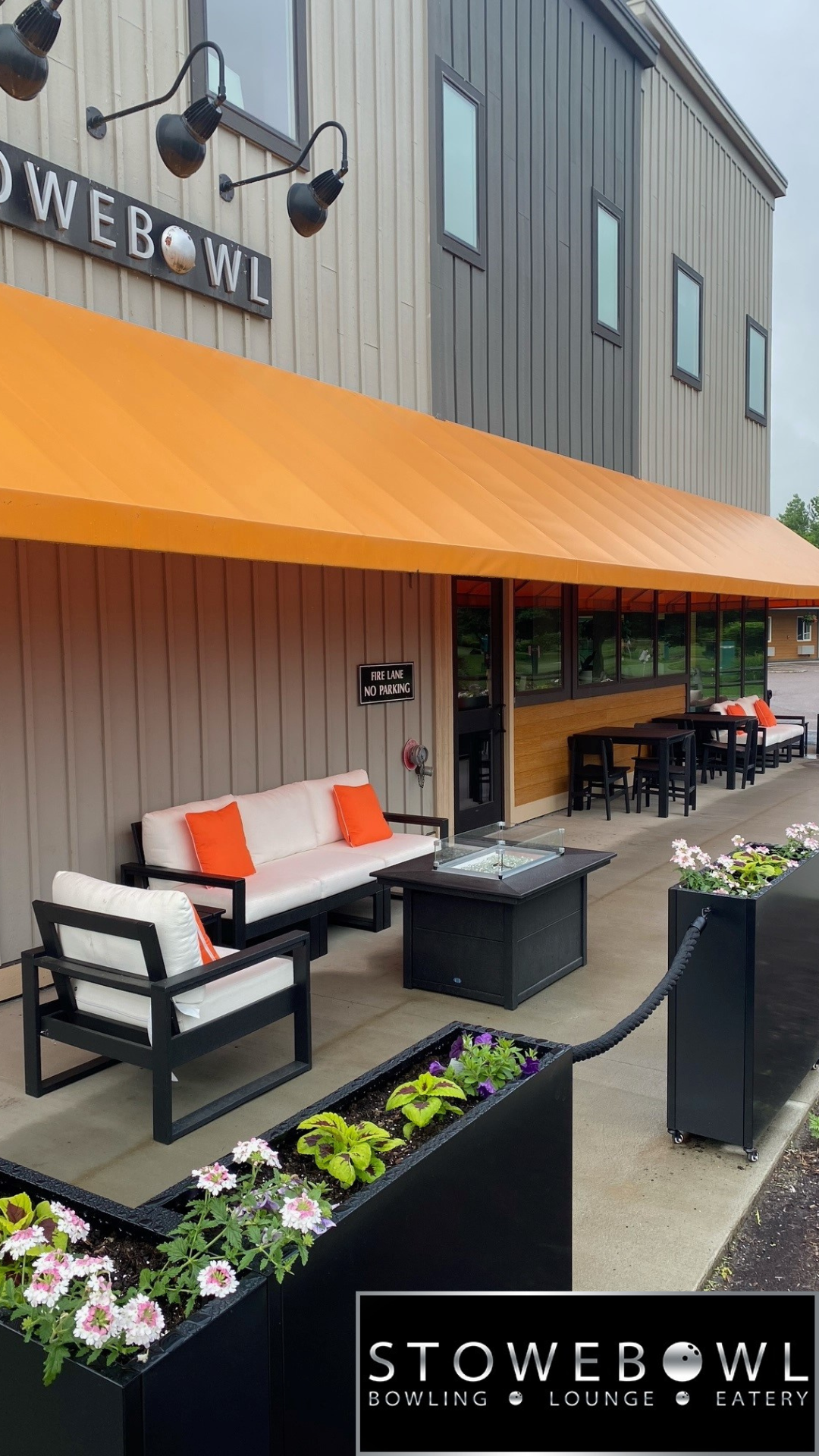 Outdoor seating with orange awning and flower planters at bowling alley.
