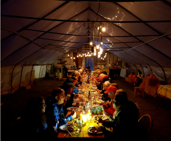 Large group dining under string lights in a spacious tent.
