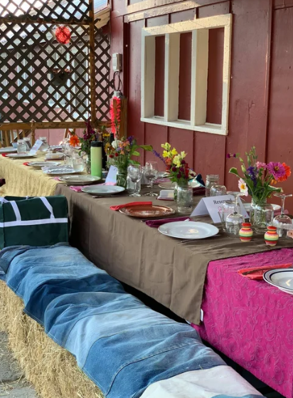 Festive outdoor dining table with colorful decor and hay bale seating.